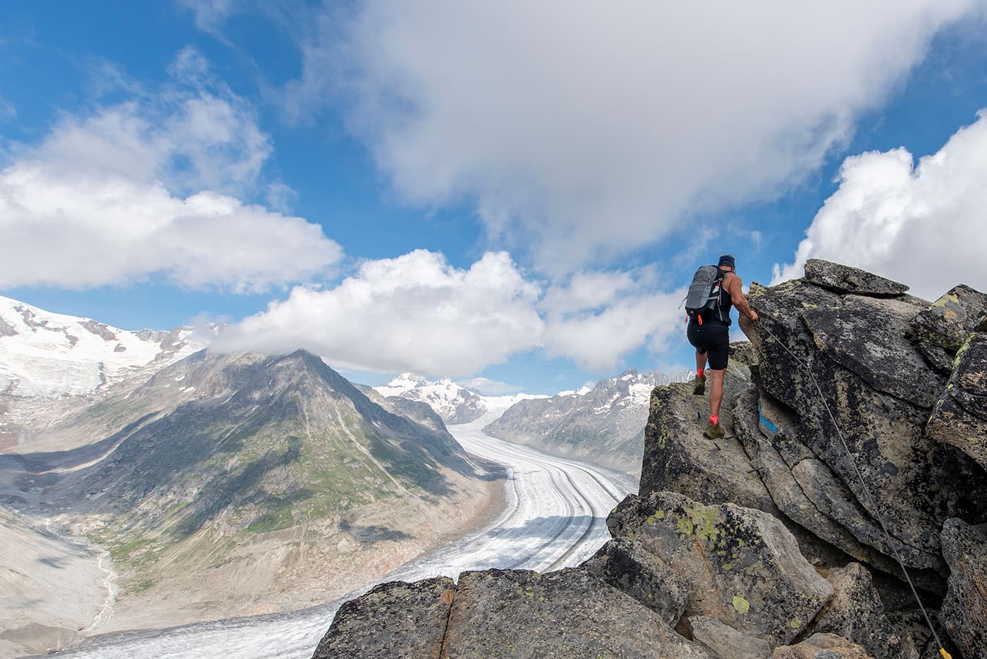 man climbing mountain top holding on to steel cables
