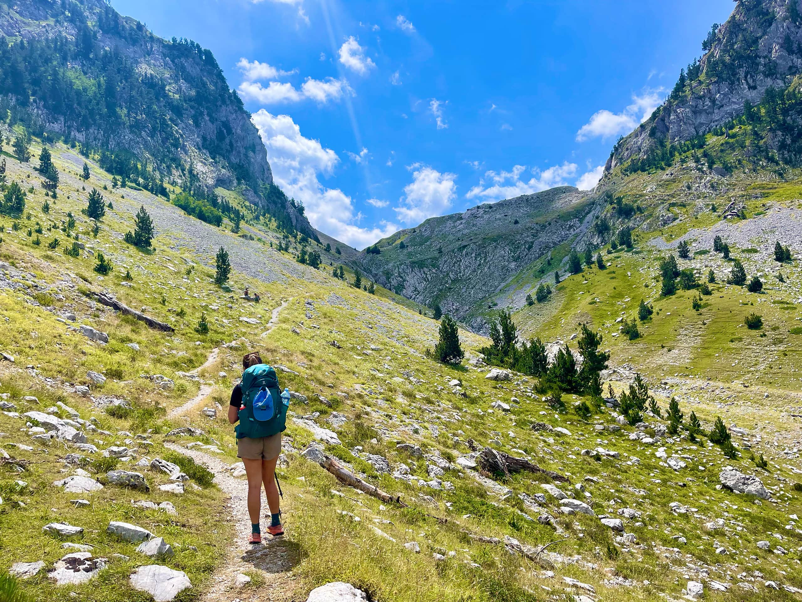Women hiking in green valley between high mountain peaks on sunny day