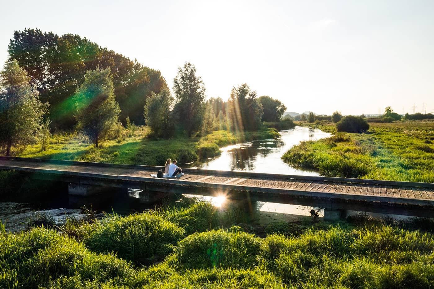 couple sitting on wooden bridge by a river
